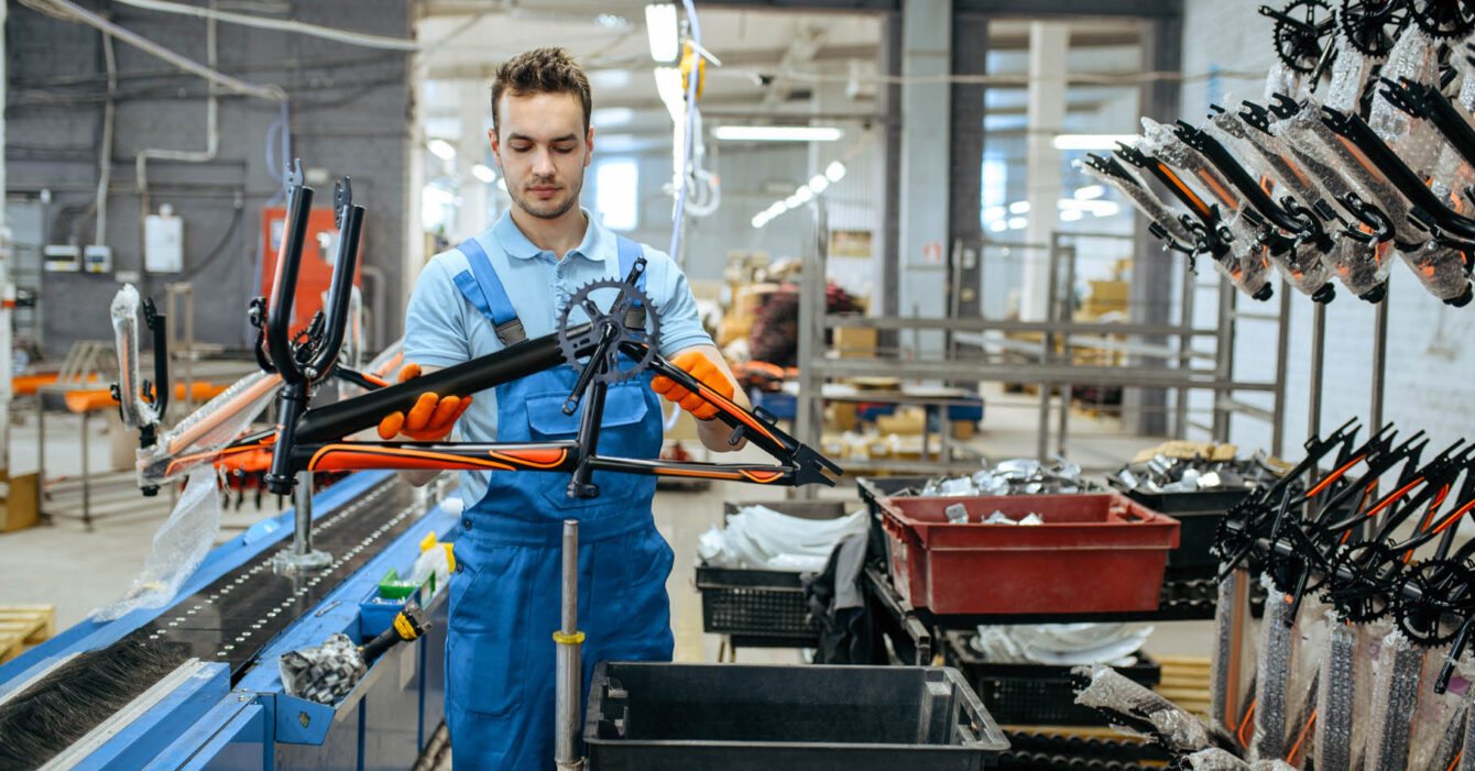 Bicycle factory, worker holds teen bike frame
